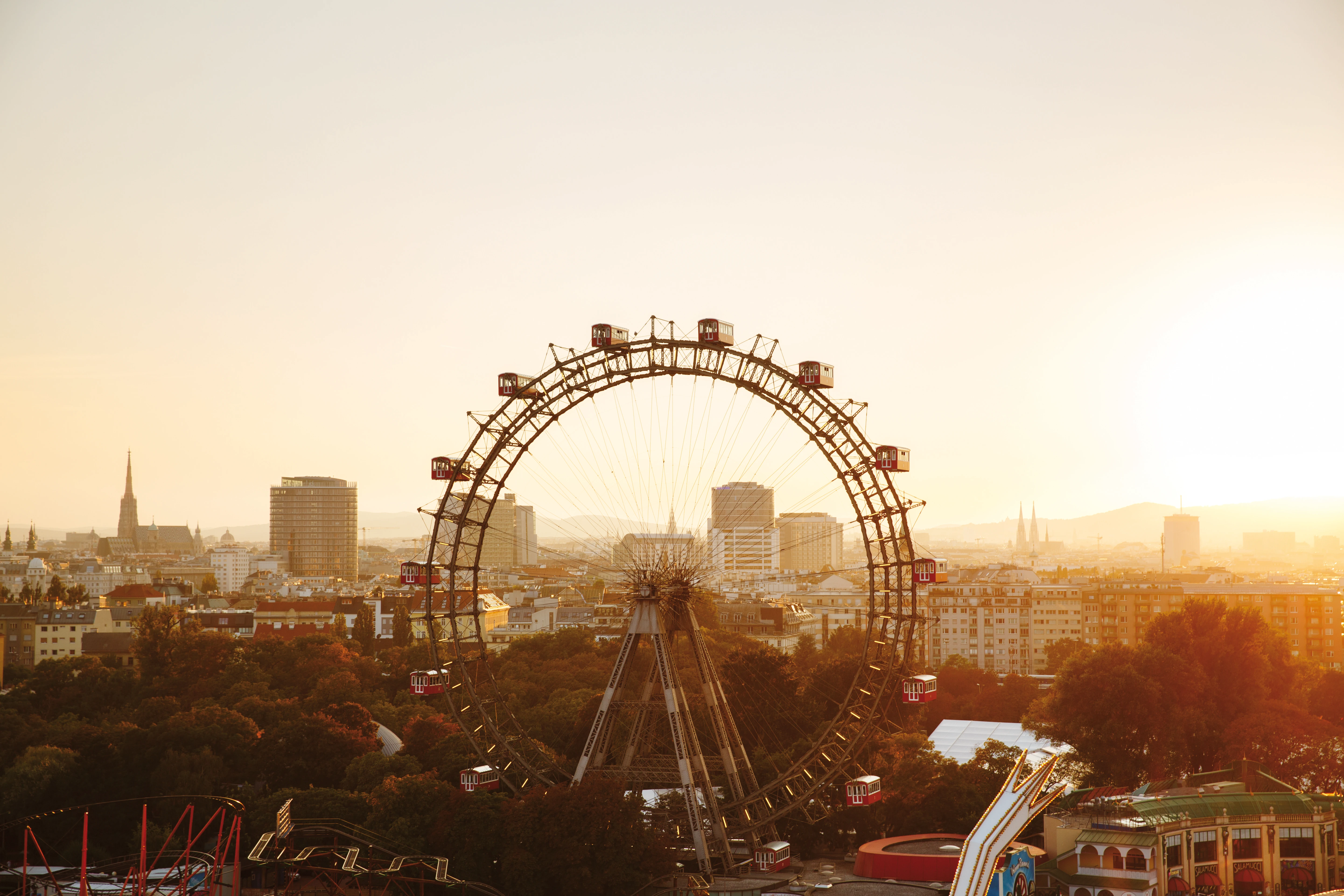 Riesenrad im Wiener Prater an einem Sommertag vor der Skyline von Wien im warmen Abendlicht.